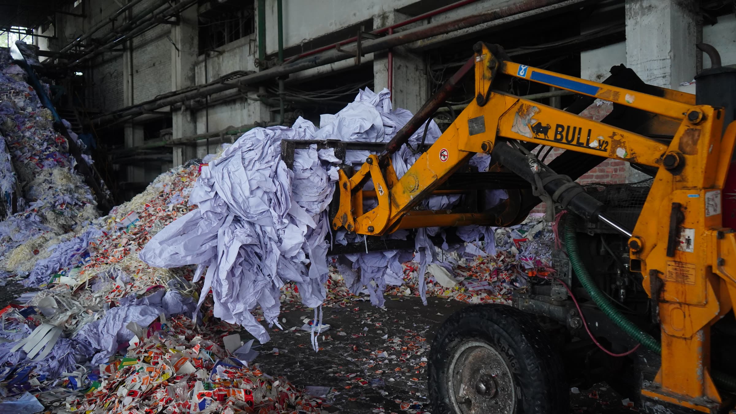 Wheeled loader lifting recovered waste paper onto the intake heap inside the mill shed