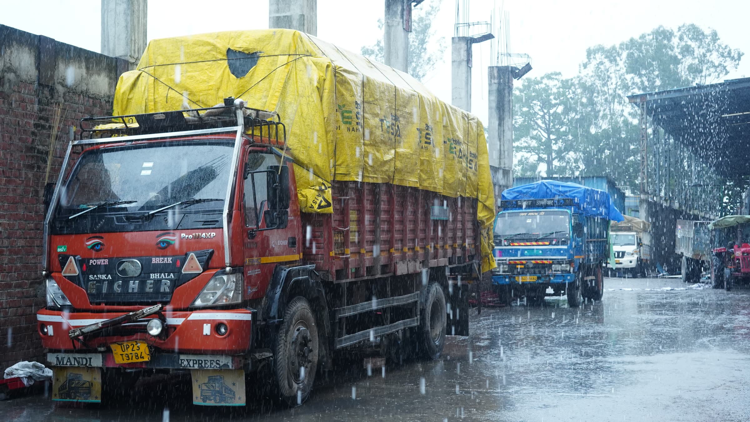 Loaded trucks queued at the Katyayini Mills gate in monsoon rain, Kashipur