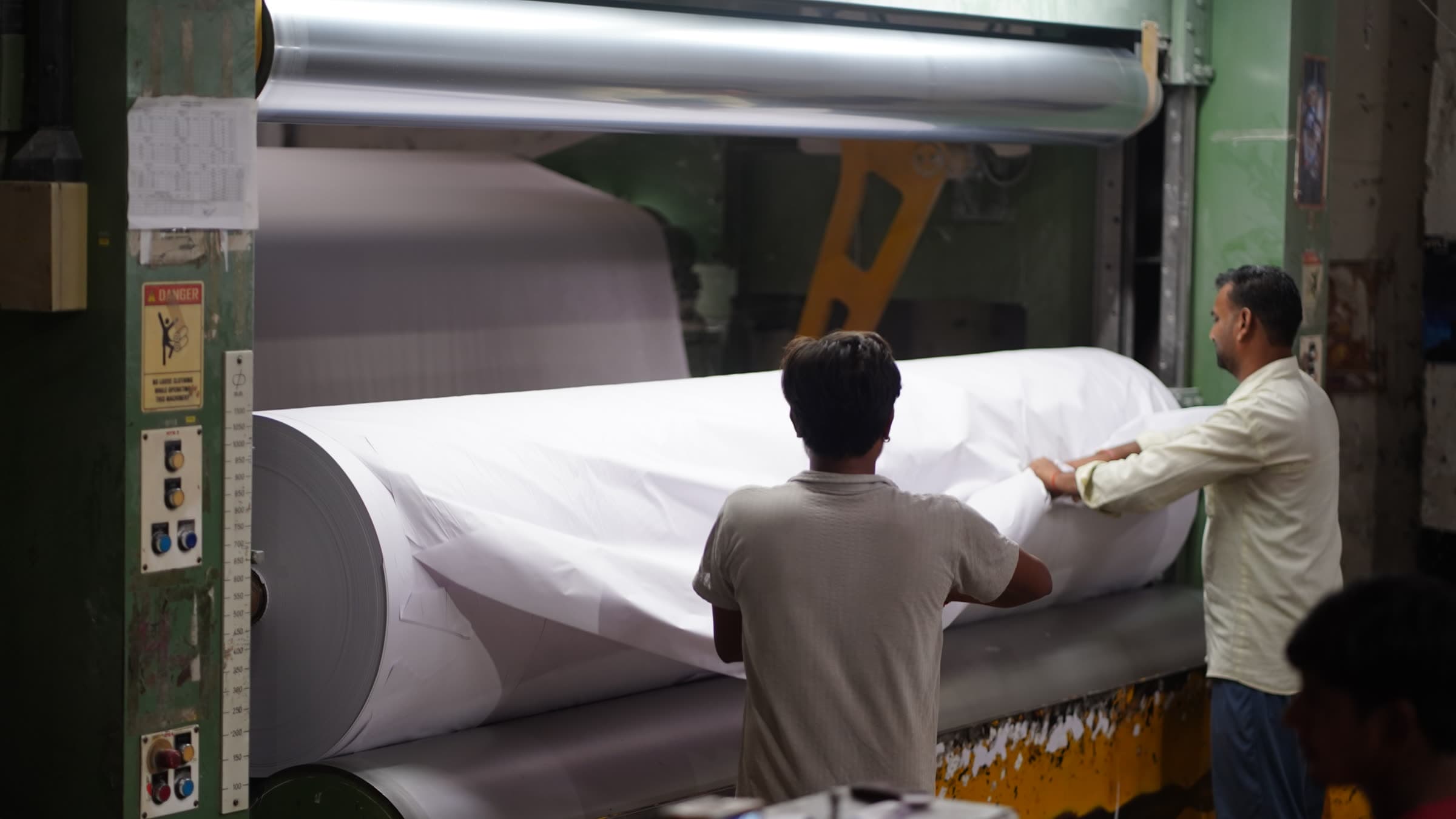 A jumbo reel building at the paper machine, operators guiding the sheet