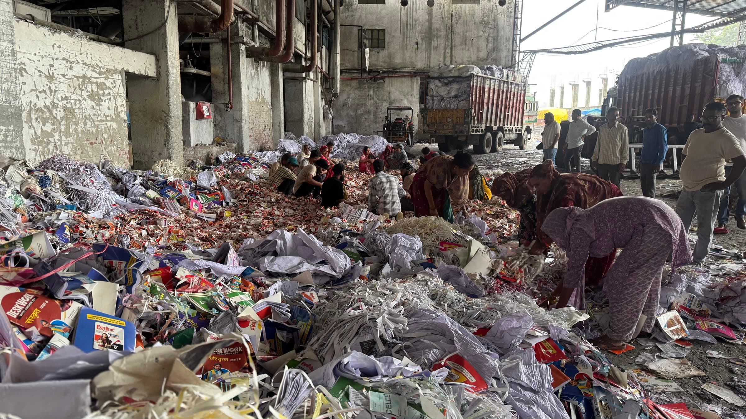 Crew sorting recovered paper across the intake shed floor, delivery trucks at the open bay behind